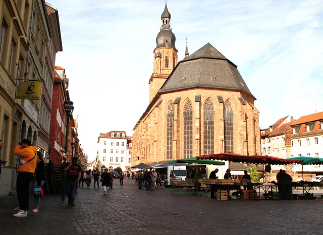 Sonniger Marktplatz in Heidelberg mit Heiliggeistkirche, historischen Häusern und Marktständen
