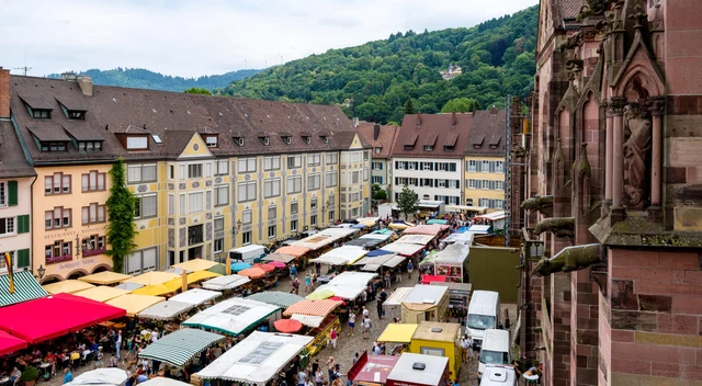 Heller Münsterplatz in Freiburg mit bunten Marktständen, historischen Fassaden und dem Münster