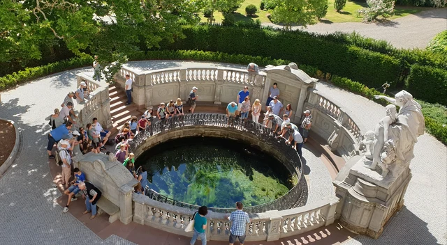 Die Donauquelle im sonnigen Schlosspark von Donaueschingen, umgeben von grünen Bäumen