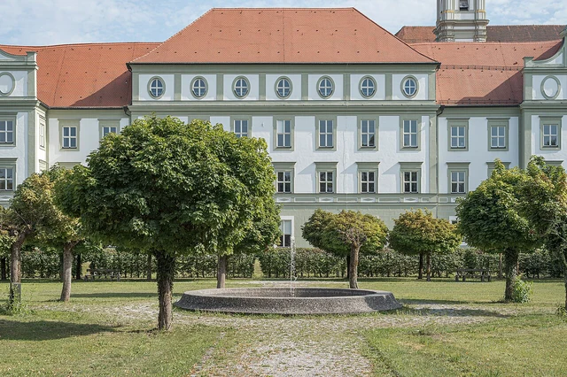 Kloster Fürstenfeld hinter Brunnen und Bäumen im Barockgarten