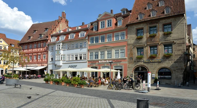 Sonniger Marktplatz in Coburg mit Fachwerkhäusern, Cafétischen und Menschen